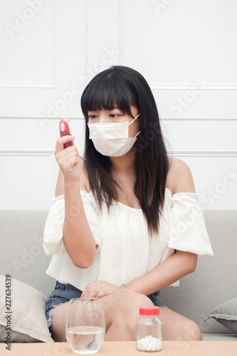 Woman suffer from cough with face mask protection and use electronic thermometer to measure body temperature.