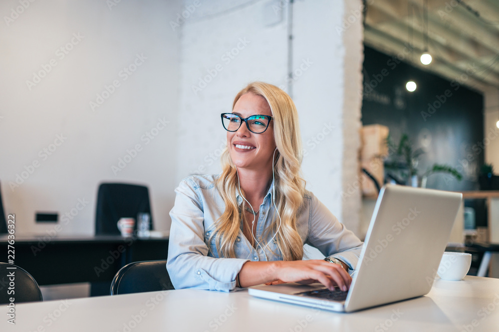 Gorgeous young woman with eyeglasses looking away while listening music and using laptop. Gorgeous young woman with eyeglasses looking away while listening music and using laptop.