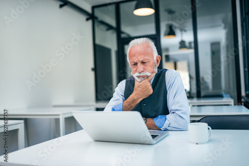 Serious senior business man looking at laptop.