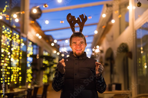 Christmas, people and winter holidays concept - surprised man in horns of deer standing at night street with bengal lights in his hands © satura_