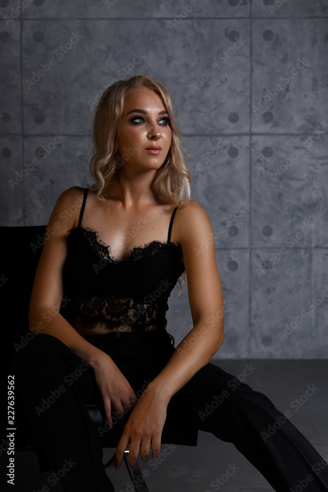 Sexy blonde girl in black lace top and pants in a dark room sitting on the couch