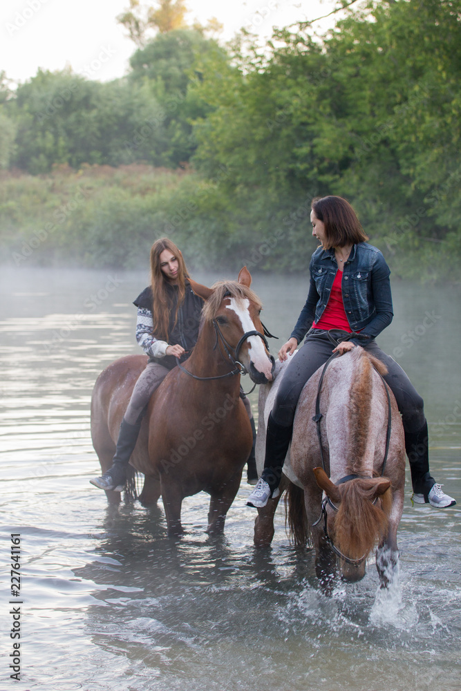 Two young women on horses stay in the water. Fog Two young women on horses stay in the water. Fog