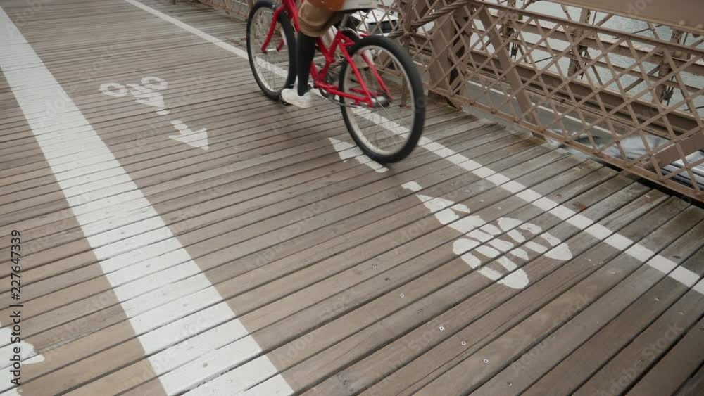 A slow motion low angle view of bicyclists in the bike lane on the Brooklyn Bridge on an overcast day.  	