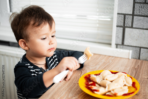 Hungry child eating dumplings in the kitchen  sitting at the table in a gray jacket