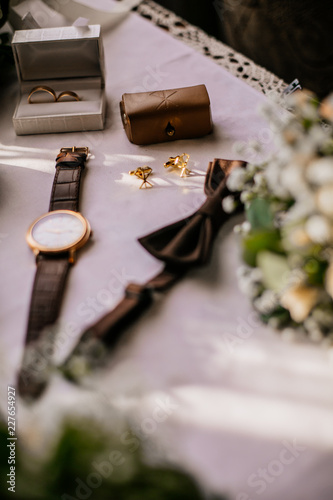 Accessories of a groom: shoes, boutonniere, tie and clock on a wooden surface