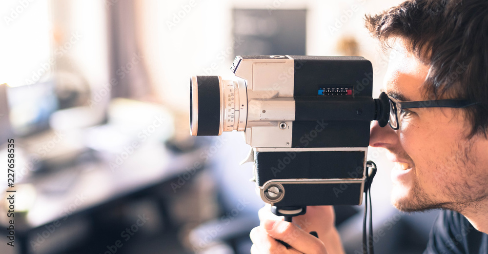 Junger Mann dreht mit Vintage/Retro-Kamera einen Film für ein Filmfestival, Breitbild - obrazy, fototapety, plakaty 