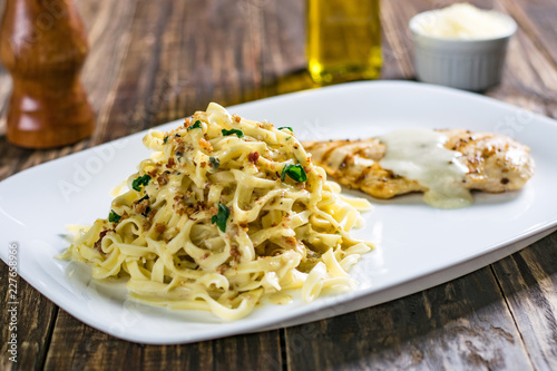 Delicious pasta with garlic and grilled chicken breast on wooden table