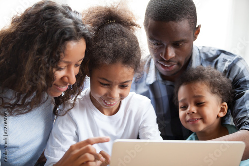 Close up black family with small children have a fun sitting on couch together at home. Happy american married couple little preschool adorable daughter and son smiling and watching on laptop screen © fizkes