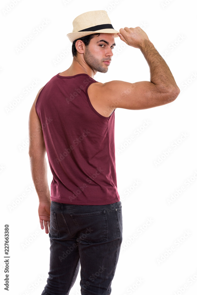 Studio shot of young handsome Hispanic man holding hat while loo Studio shot of young handsome Hispanic man holding hat while loo