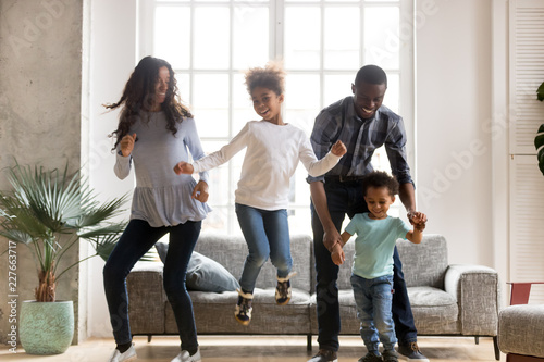 Full length black African whole family have a fun. Married couple with little kids toddler son preschool daughter dancing moving in living room at new home. Happy family spend time together concept