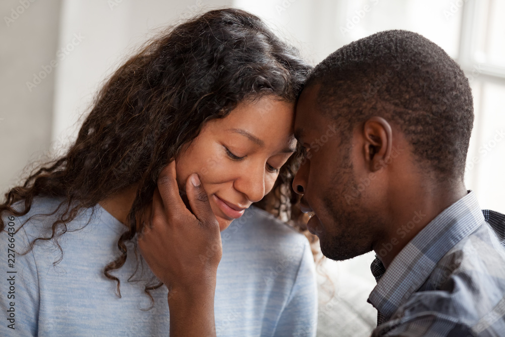 Close up portrait of black african couple in love together at home. American male gently touch face of beloved female enjoy company of each other having romantic date. Feelings and first kiss concept Close up portrait of black african couple in love together at home. American male gently touch face of beloved female enjoy company of each other having romantic date. Feelings and first kiss concept