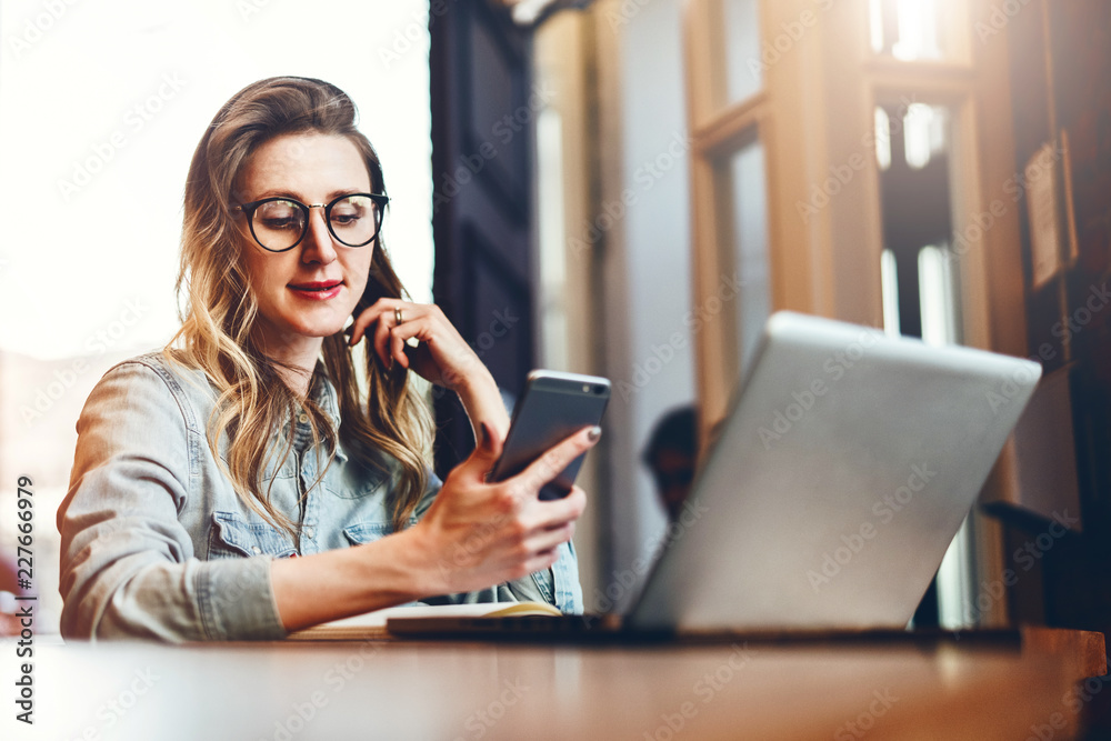 Young businesswoman is sitting in coffee shop at table in front of computer and notebook,using smartphone. Social media. Young businesswoman is sitting in coffee shop at table in front of computer and notebook,using smartphone. Social media.