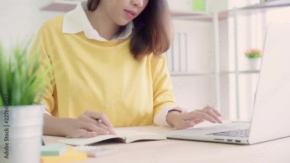 Beautiful young smiling asian woman working laptop on desk in living room at home. Asia business woman writing notebook document finance and calculator in home office. Enjoying time at home concept. Beautiful young smiling asian woman working laptop on desk in living room at home. Asia business woman writing notebook document finance and calculator in home office. Enjoying time at home concept.