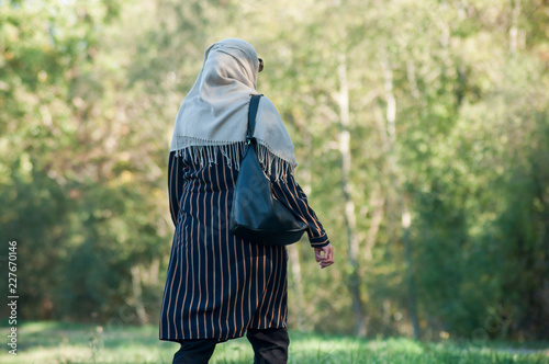 Portrait of Veiled Muslim woman walking in public garden on back view