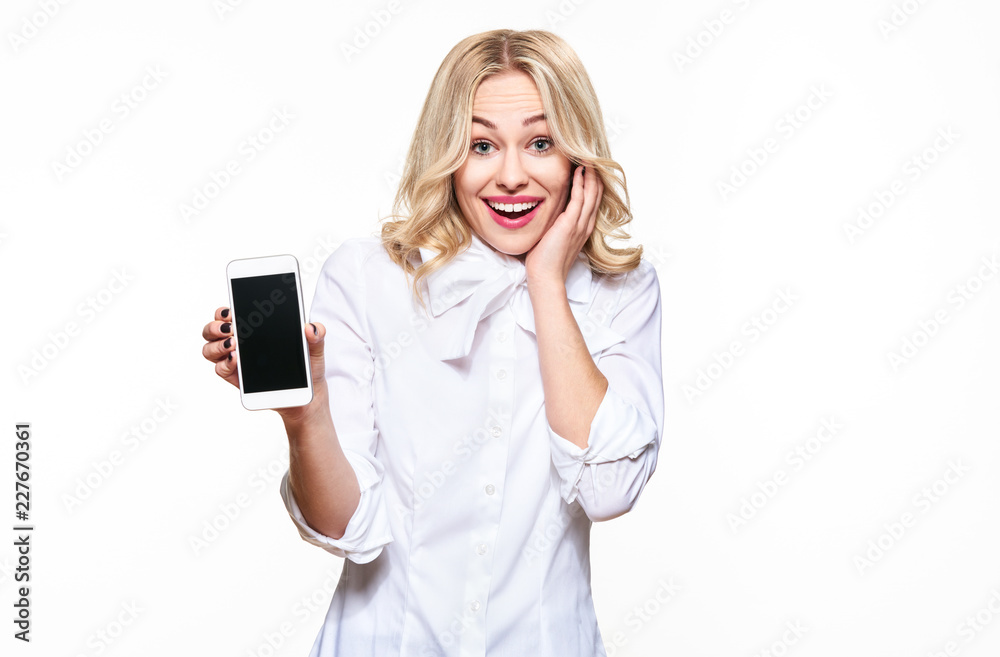Gorgeous excited woman showing blank screen mobile phone over white background, celebrating victory and success. Very excited, cheering emotion.