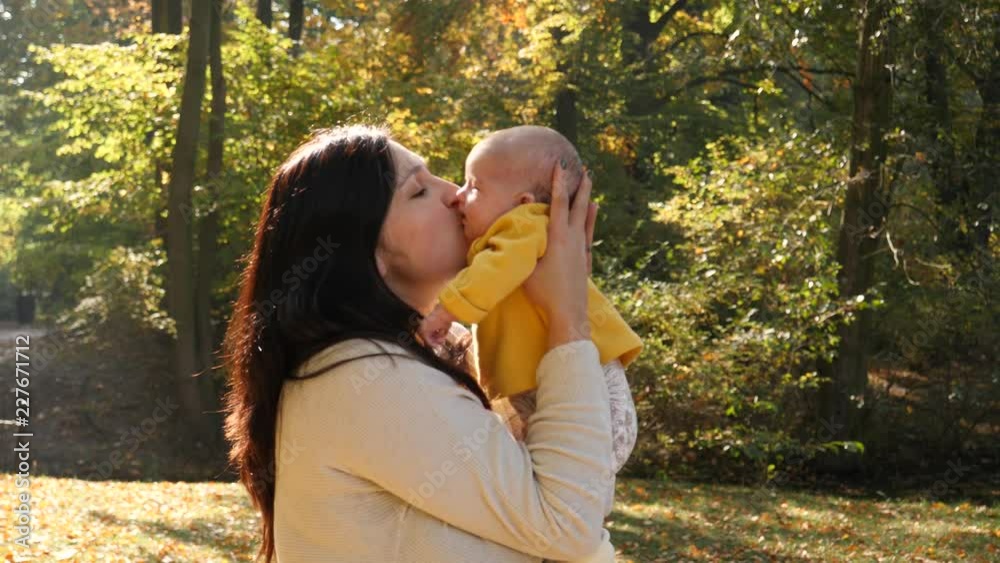 Mother tenderly hold and kisses her infant baby daughter in sun light in autumn park Mother tenderly hold and kisses her infant baby daughter in sun light in autumn park