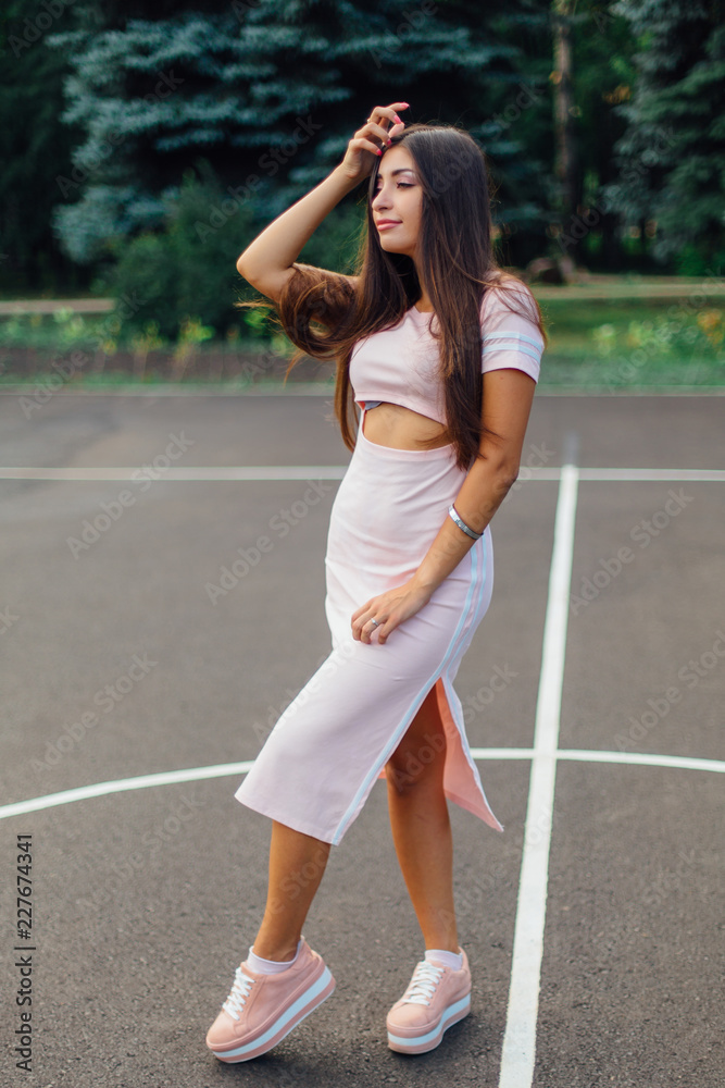 Charming brunette female dressed in a pink dress posing on the basketball court. Charming brunette female dressed in a pink dress posing on the basketball court.
