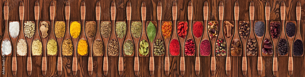 Spices and herbs from different countries in wooden spoons. Colorful seasonings on   table background, top view. - obrazy, fototapety, plakaty 