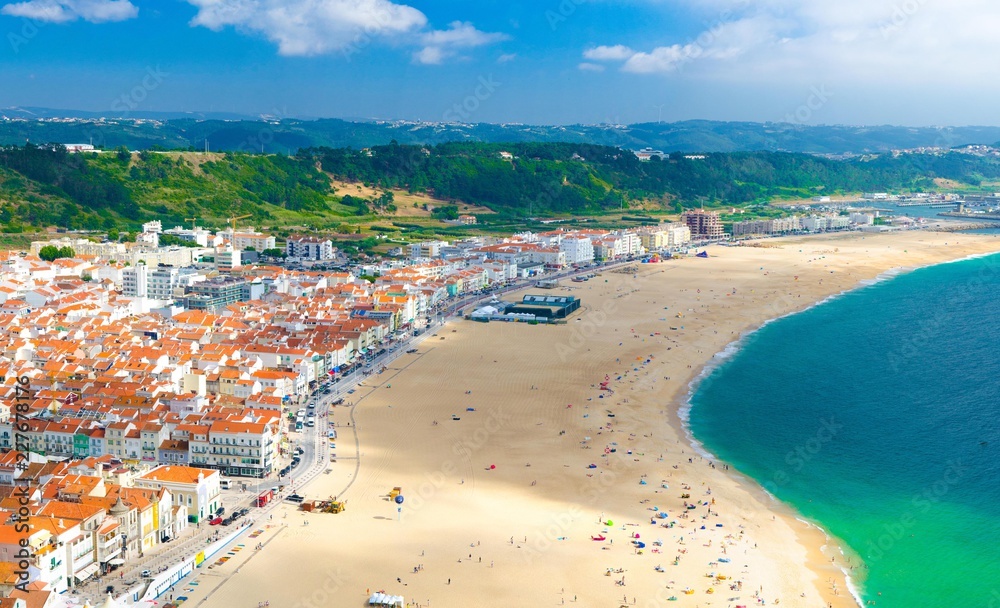 Aerial panoramic view of Nazare city town with wide gold sandy beach and white houses with tiled roofs on the Atlantic ocean coast from top platform, Portugal