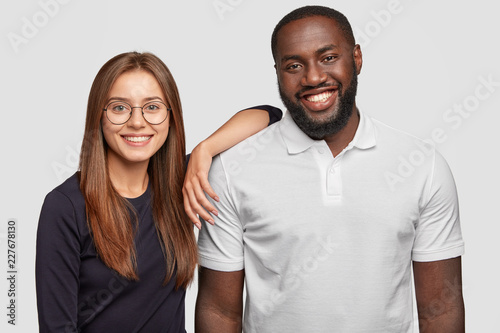 Photo of cheerful lovely diverse couple smile positively, stand next to each ...