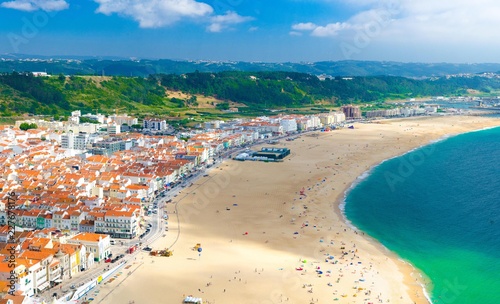Aerial panoramic view of Nazare city town with wide gold sandy beach and white houses with tiled roofs on the Atlantic ocean coast from top platform, Portugal