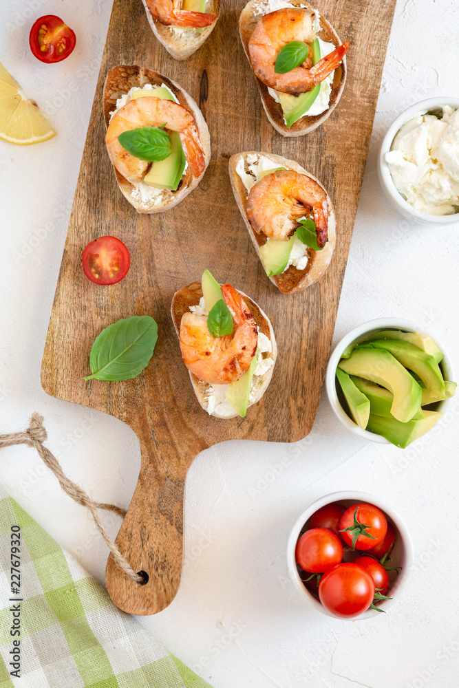 Bruschetta italian snack sandwiches with shrimps, avocado and cheese decorated by basil.