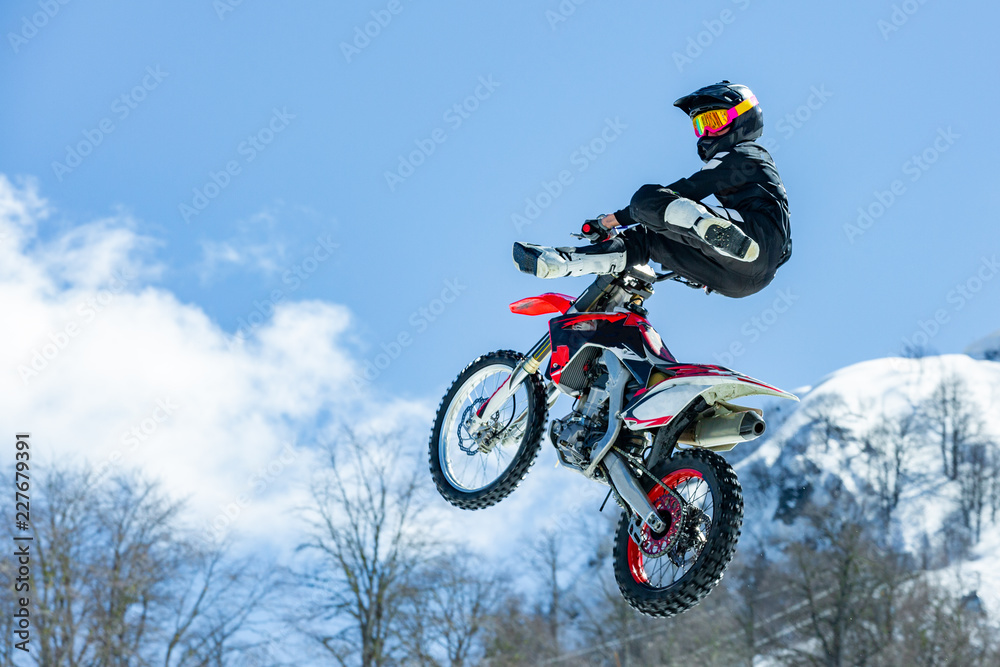 racer on a motorcycle in flight, jumps and takes off on a springboard against the snowy mountains racer on a motorcycle in flight, jumps and takes off on a springboard against the snowy mountains