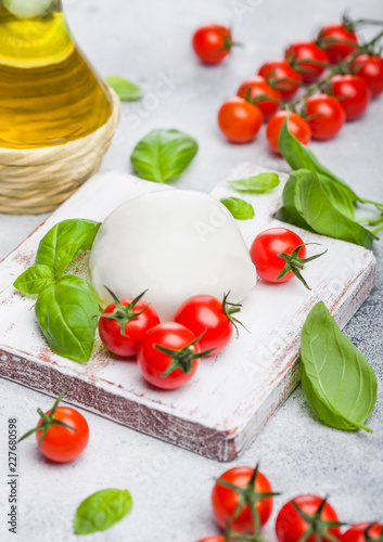 Fresh Mozzarella cheese on vintage chopping board with tomatoes and basil leaf with olive oil on stone kitchen table background.