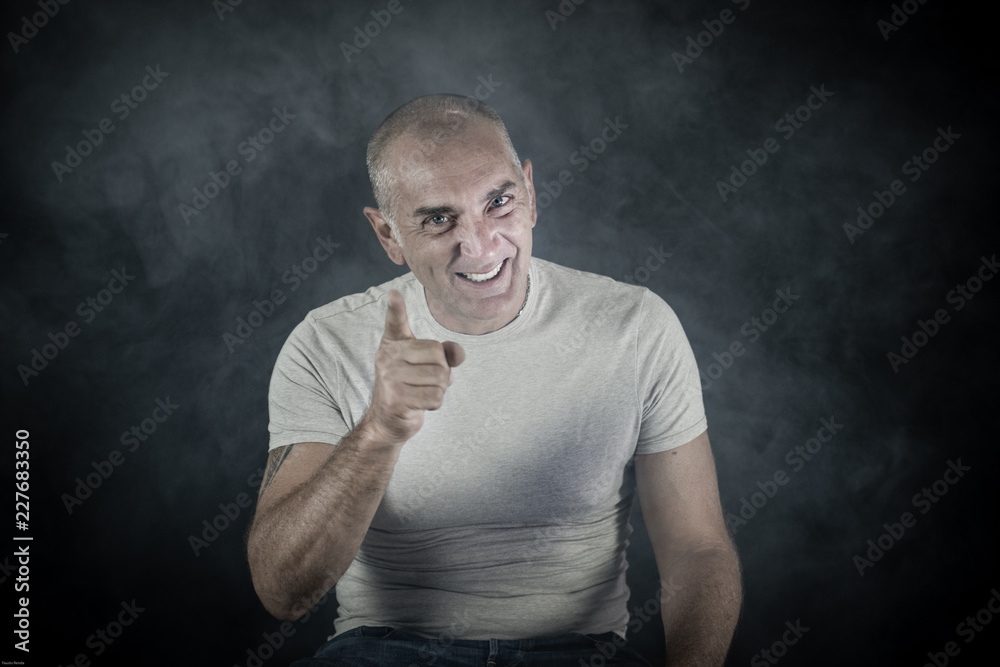 A man, 50Y old, is showing the index of the right hand. Black background. Smoke