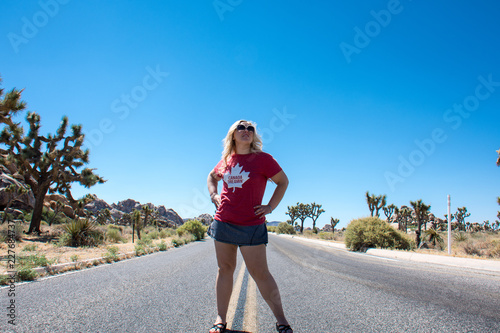Young adult woman stands in the middle of a lone desert highway in Joshua Tree National Park, concept for powerful, freedom, adventure