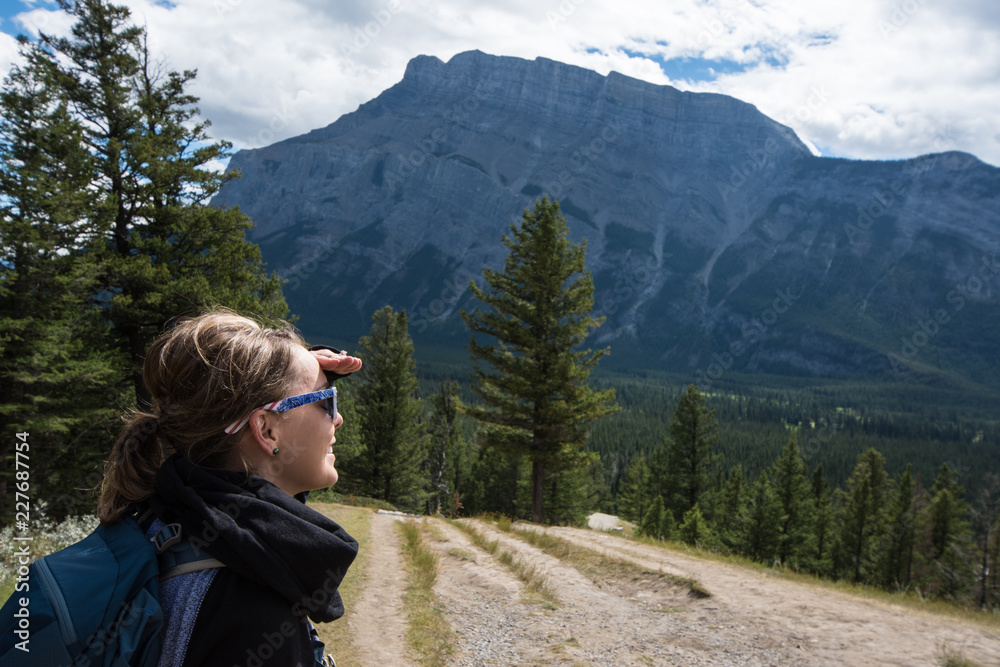 Young woman backpacker hiker looks out at the view of Banff National Park in Canada, enjoying the scenic Canadian Rockies