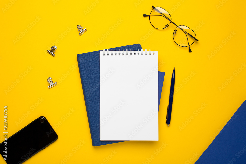White notepad with blue notebook and pen on yellow background White notepad with blue notebook and pen on yellow background