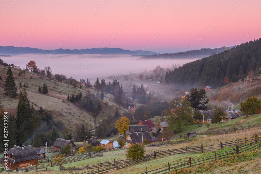 Small village in the mountains during autumn at sunrise with fog