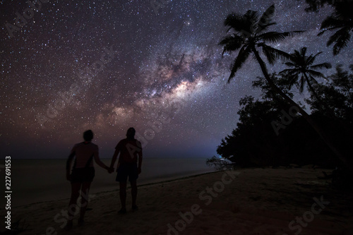Silhouette of couple gazing and enjoying the view of milky way on the beach of Zanzibar with palm trees in background. Tanzania