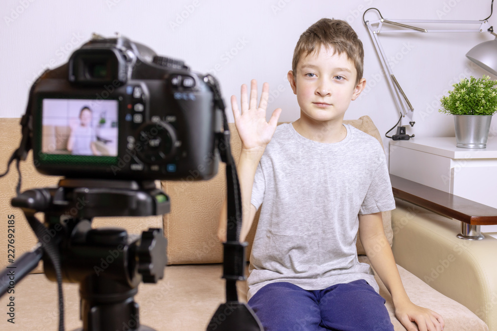A boy, male child video blogger recording vlog or podcast, streaming online. Blurred camera on tripod in front A boy, male child video blogger recording vlog or podcast, streaming online. Blurred camera on tripod in front