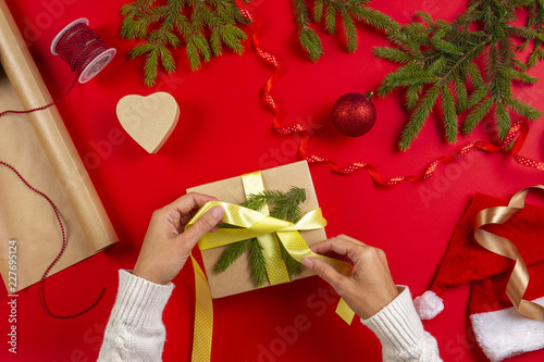 Christmas gift wrapping. Woman's hands packing Christmas present box on red table background photo