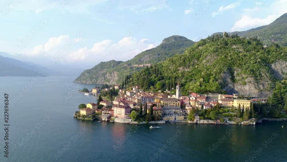 High top view old Italy town on bank of Como lake. Flying above water landscape with green hills and town afar. Varenna, Italy