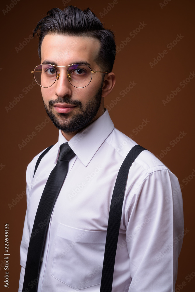 Young handsome bearded Iranian businessman against brown backgro Young handsome bearded Iranian businessman against brown backgro