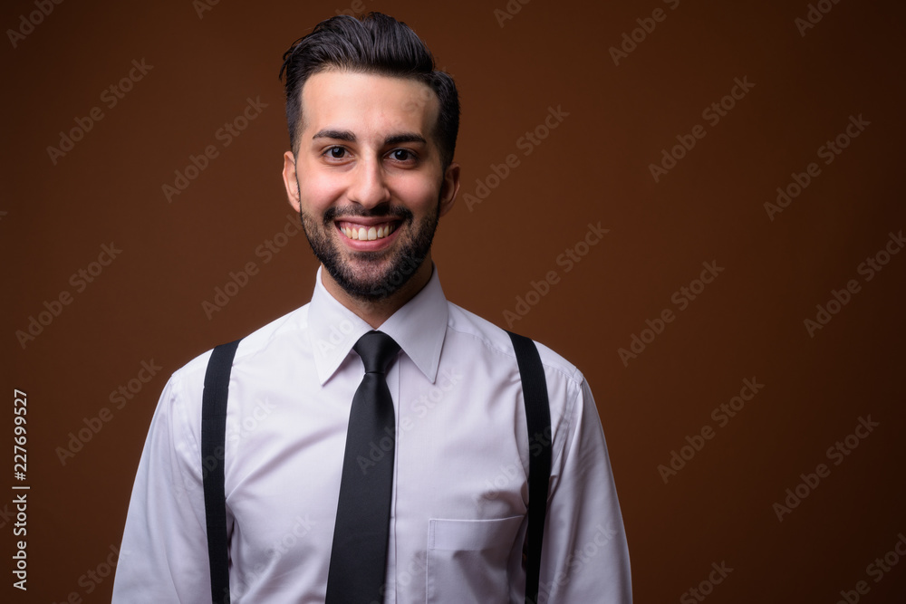 Young handsome bearded Iranian businessman against brown backgro Young handsome bearded Iranian businessman against brown backgro
