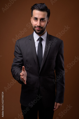 Young handsome bearded Iranian businessman against brown backgro