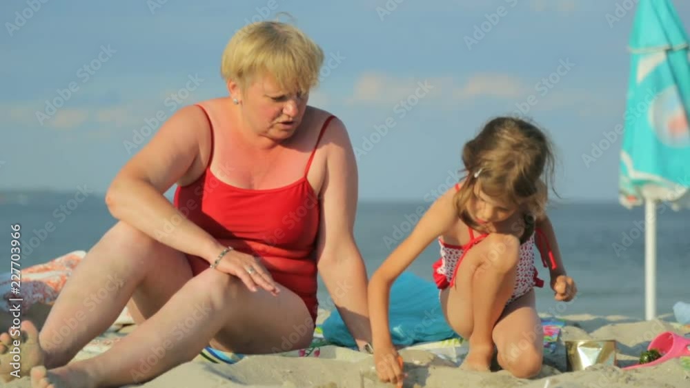 Woman with little girl playing with sand on beach Woman with little girl playing with sand on beach