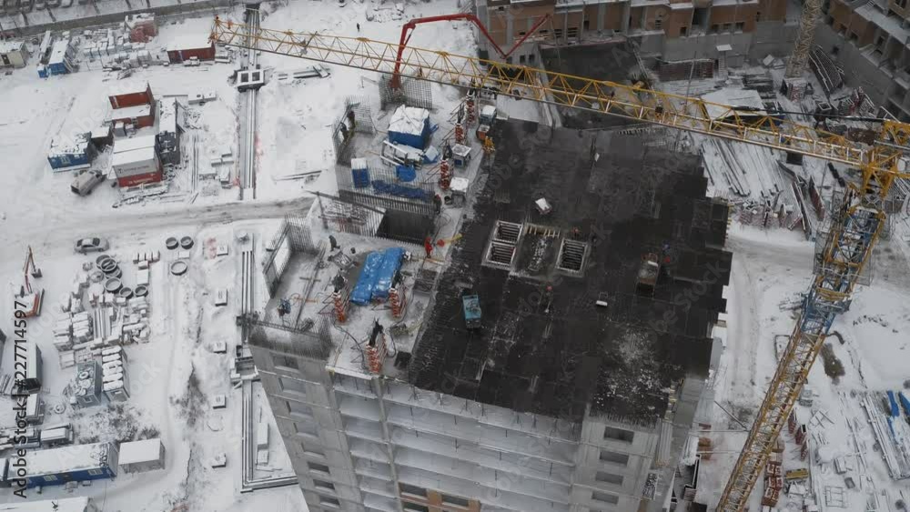 Aerial drone shot: Apartment building construction site, development of new areas, workers at the top, building new house, creation of new jobs, construction crane moves materials, winter cloudy Aerial drone shot: Apartment building construction site, development of new areas, workers at the top, building new house, creation of new jobs, construction crane moves materials, winter cloudy