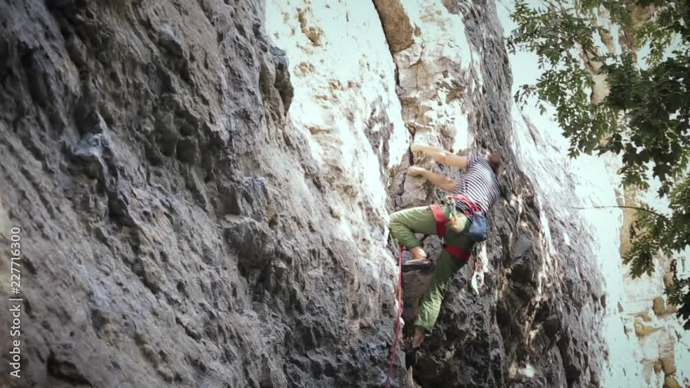 side view of woman rock climber in bright green pants climbing on the cliff. rock climber climbs on a rocky wall. woman making hard move side view of woman rock climber in bright green pants climbing on the cliff. rock climber climbs on a rocky wall. woman making hard move
