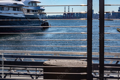 Looking through a guardrail at a docked yacht on a sunny day.