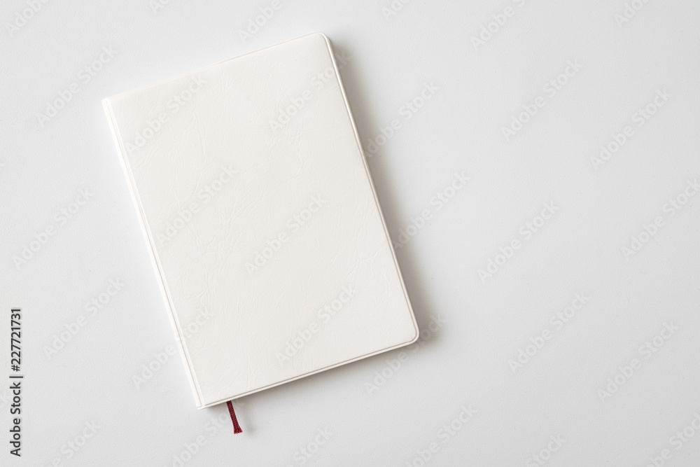 Top view of closed blank white leather cover notebook on white desk background with copy space Top view of closed blank white leather cover notebook on white desk background with copy space