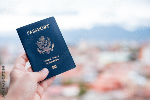 One single hand holding a blue American passport in front of a blurry background