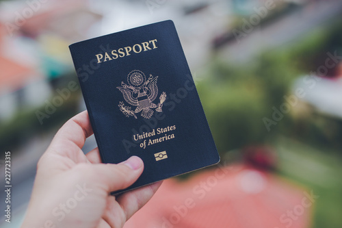 One single hand holding a blue American passport in front of a blurry background