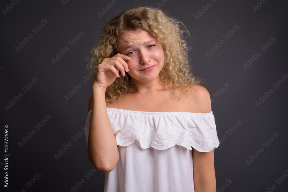 Young beautiful woman with blond curly hair against gray backgro
