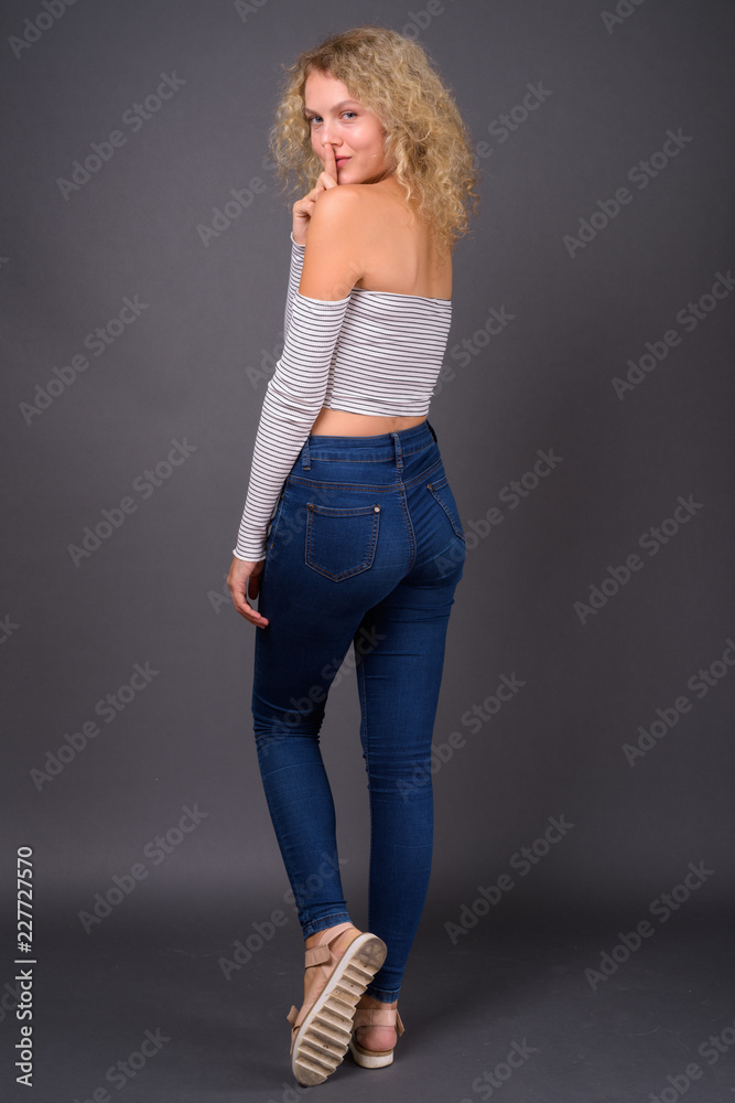 Young beautiful woman with blond curly hair against gray backgro Young beautiful woman with blond curly hair against gray backgro