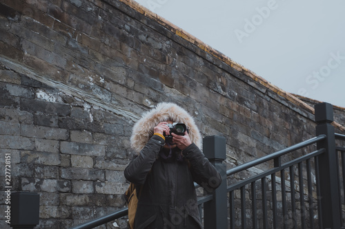 Asian woman wear coat take a photo with camera at wall in winter season,